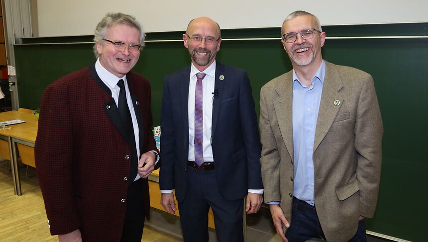 three older men standing in front of a lecture boards