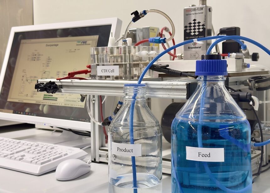 Laboranlage mit Schläuchen, Behältern für Feed- und Produktlösung sowie Computersteuerung auf einem Labortisch.